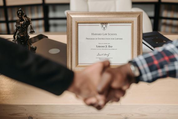 Handshake over a desk with a framed certificate in the background