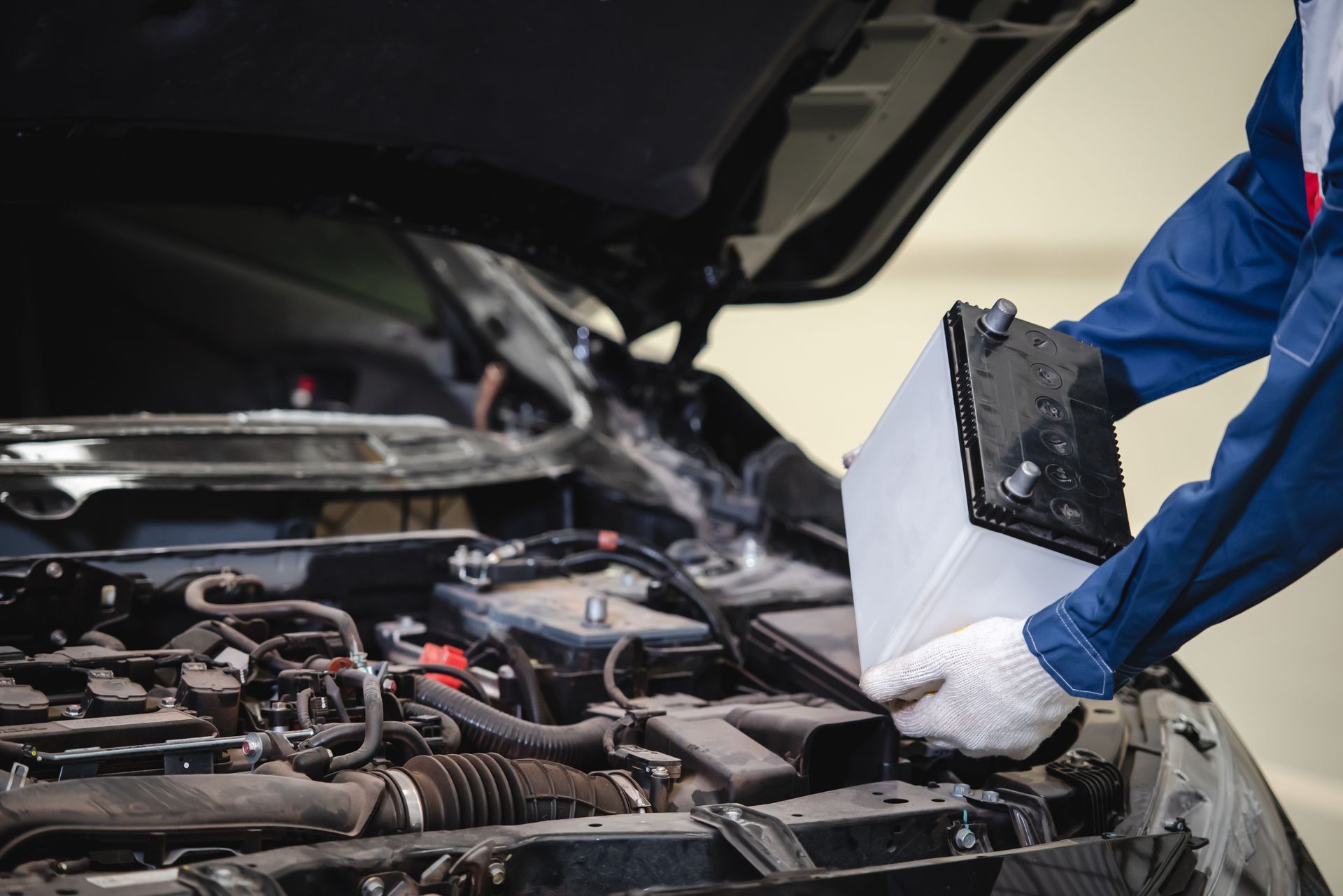 Mechanic holding a car battery beside an open car hood in a garage | Quality Auto Center