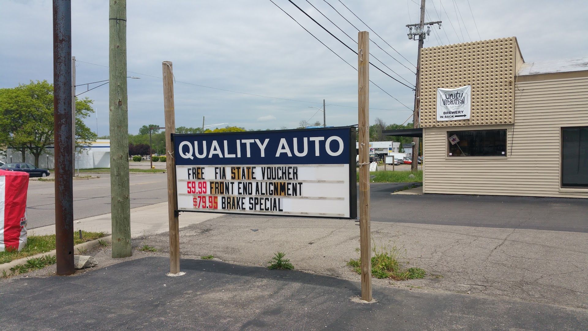Quality Auto roadside sign beside a beige building and parking lot under overcast skies | Quality Auto Center