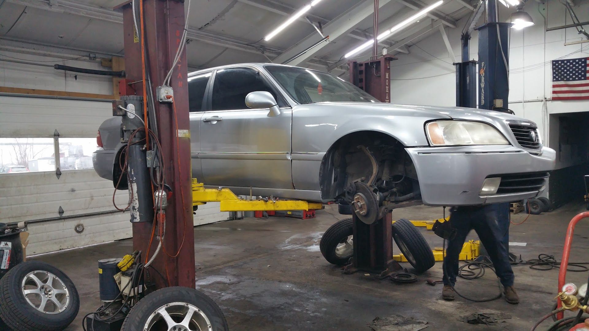 Silver sedan on a lift in an auto shop while two mechanics work underneath | Quality Auto Center