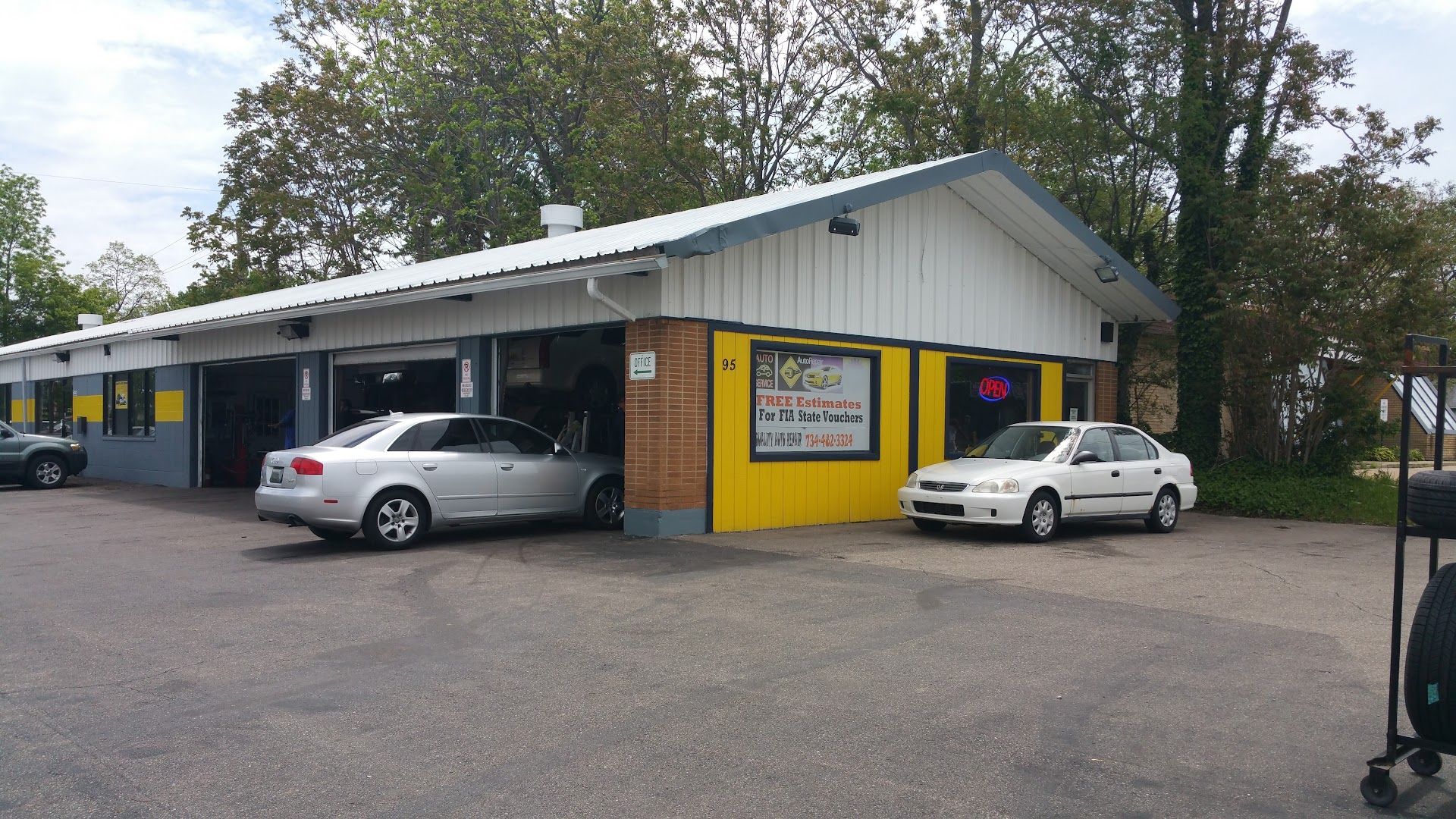 Small auto repair shop with open bays, two parked cars, and a yellow-and-white exterior. | Quality Auto Center