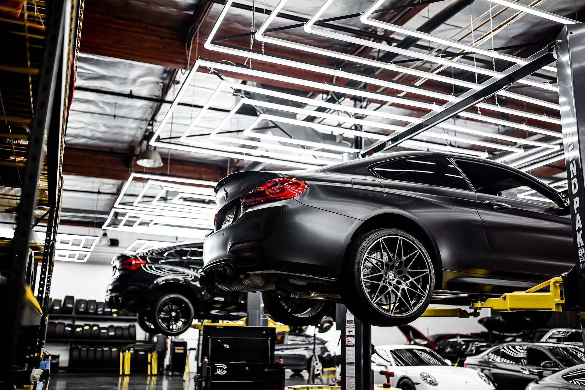 Black sports car lifted in a brightly lit auto repair shop with another car in the background | Quality Auto Center