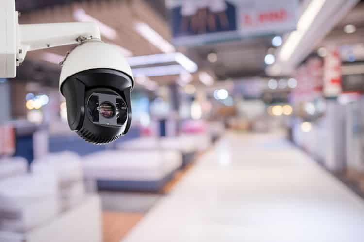 Security Camera in a Store, White and Black, Mounted on a Wall, Blurred Store Interior in the Background — IRIS CCTV in Woolgoolga, NSW