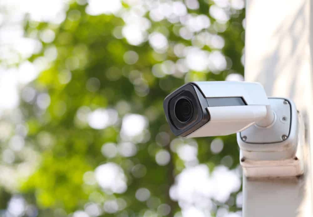 Security Camera Mounted on a White Wall With a Blurred Green Tree Background — IRIS CCTV in Yamba, NSW