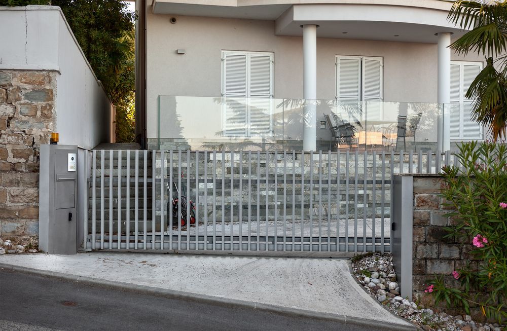 Gray Metal Gate in Front of a Light-colored House With White Shutters, Driveway, and a Glass Barrier — IRIS CCTV in South Grafton, NSW