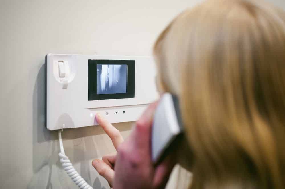 Woman Uses a Video Intercom, Pushing a Button While Holding the Handset to Her Ear — IRIS CCTV in South Grafton, NSW