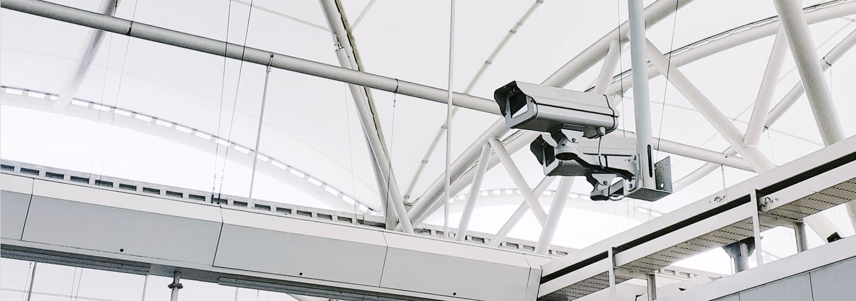 Two Security Cameras Hanging From a White, Geometric Ceiling in a Large Building — IRIS CCTV in Lismore, NSW