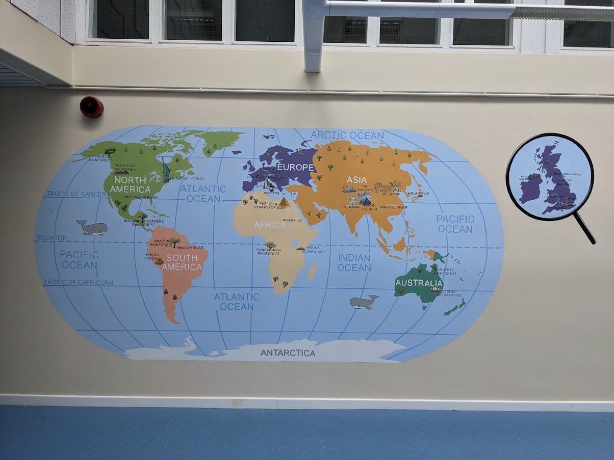hand painted world map mural in a primary school with some key landmarks and the UK highlighted with a magnifying glass
