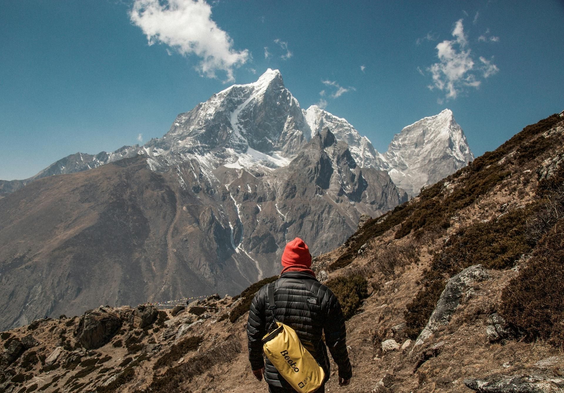 Hiker with yellow backpack trekking toward snowy mountain peaks under a blue sky