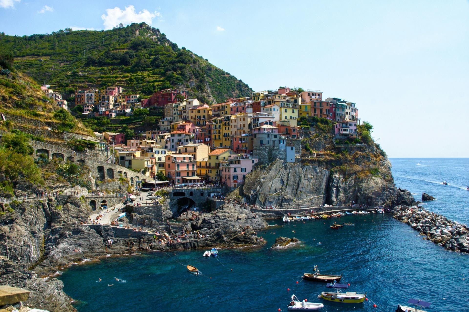 Colorful cliffside village overlooking a blue Mediterranean harbor with boats and rocky shoreline