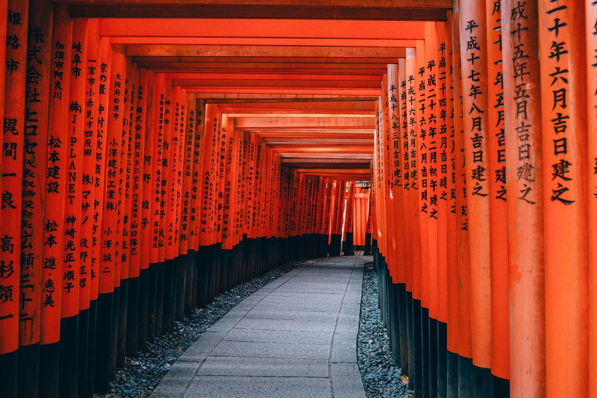 Red-orange torii gates lining a narrow stone path, forming a tunnel-like shrine walkway.