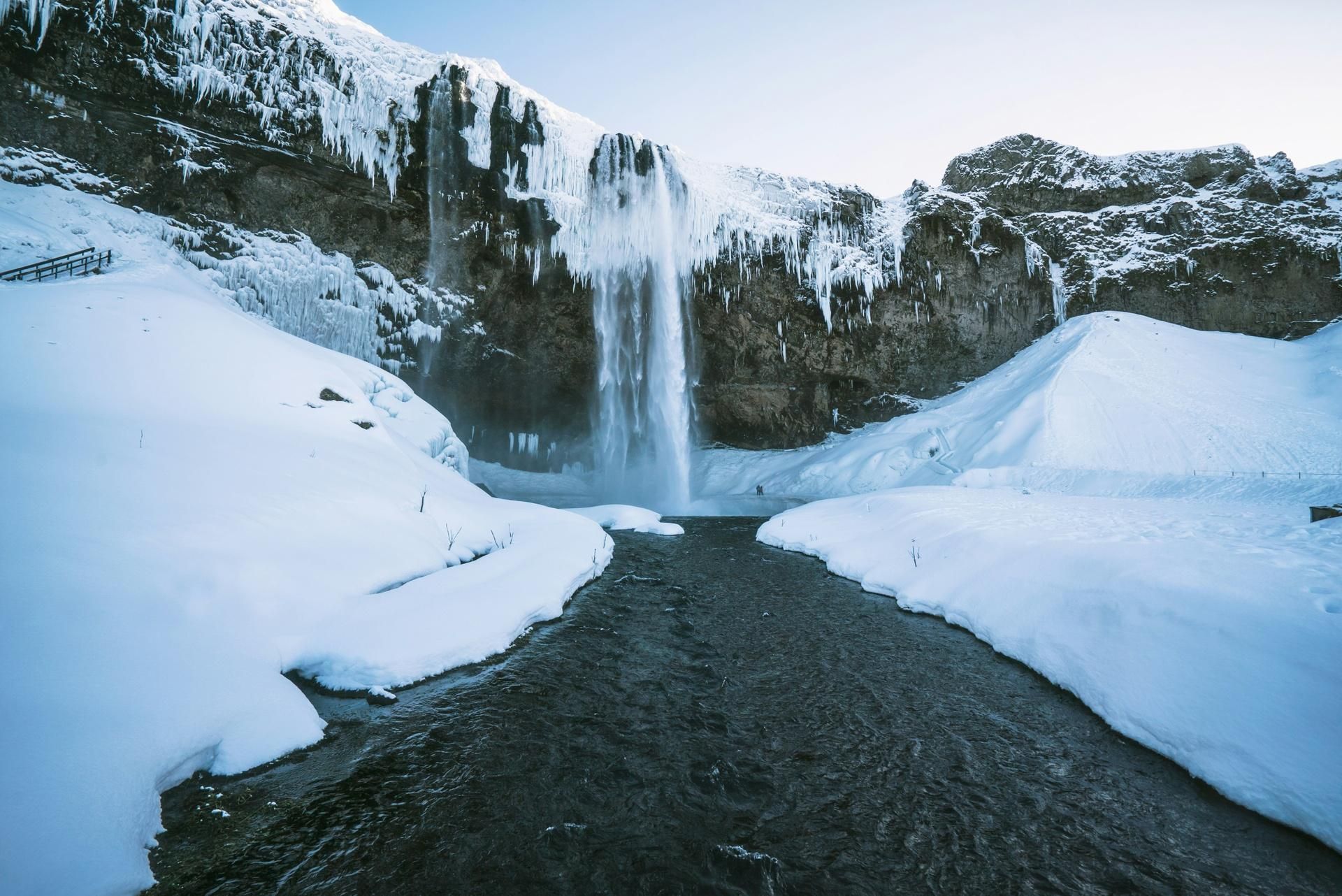 Snowy canyon with a waterfall flowing into a dark river under icy cliffs