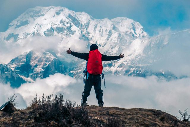 Person in a red jacket stands with arms outstretched before snow-covered mountains.