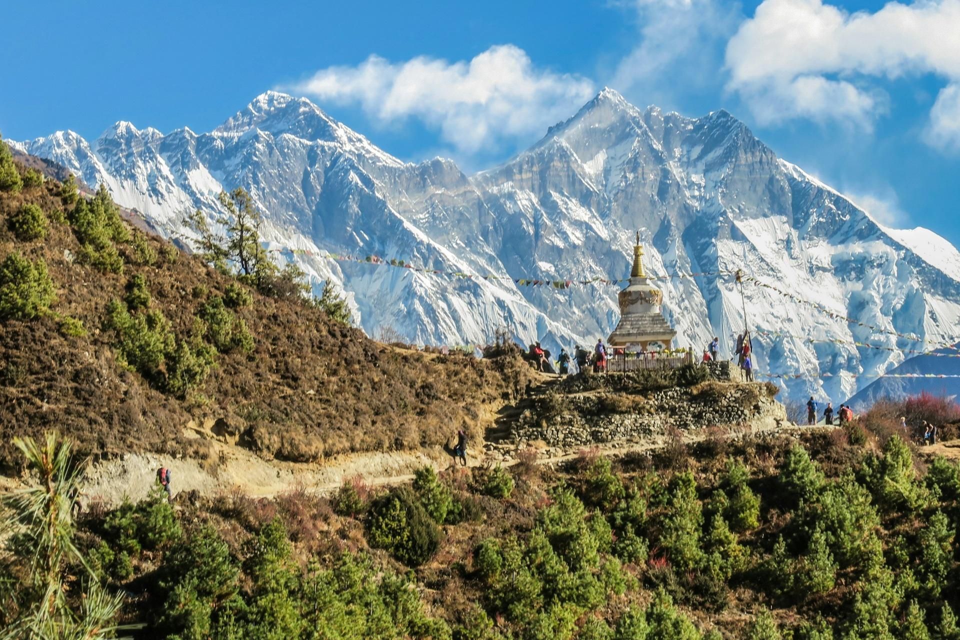 Snowy mountains behind a hilltop monastery and winding dirt road under a blue sky