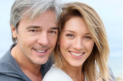 Two smiling adults with light hair posing closely against a soft blue background