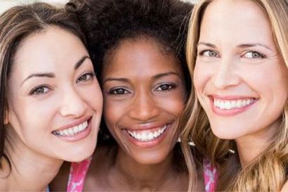 Three smiling women posing closely together against a light background.