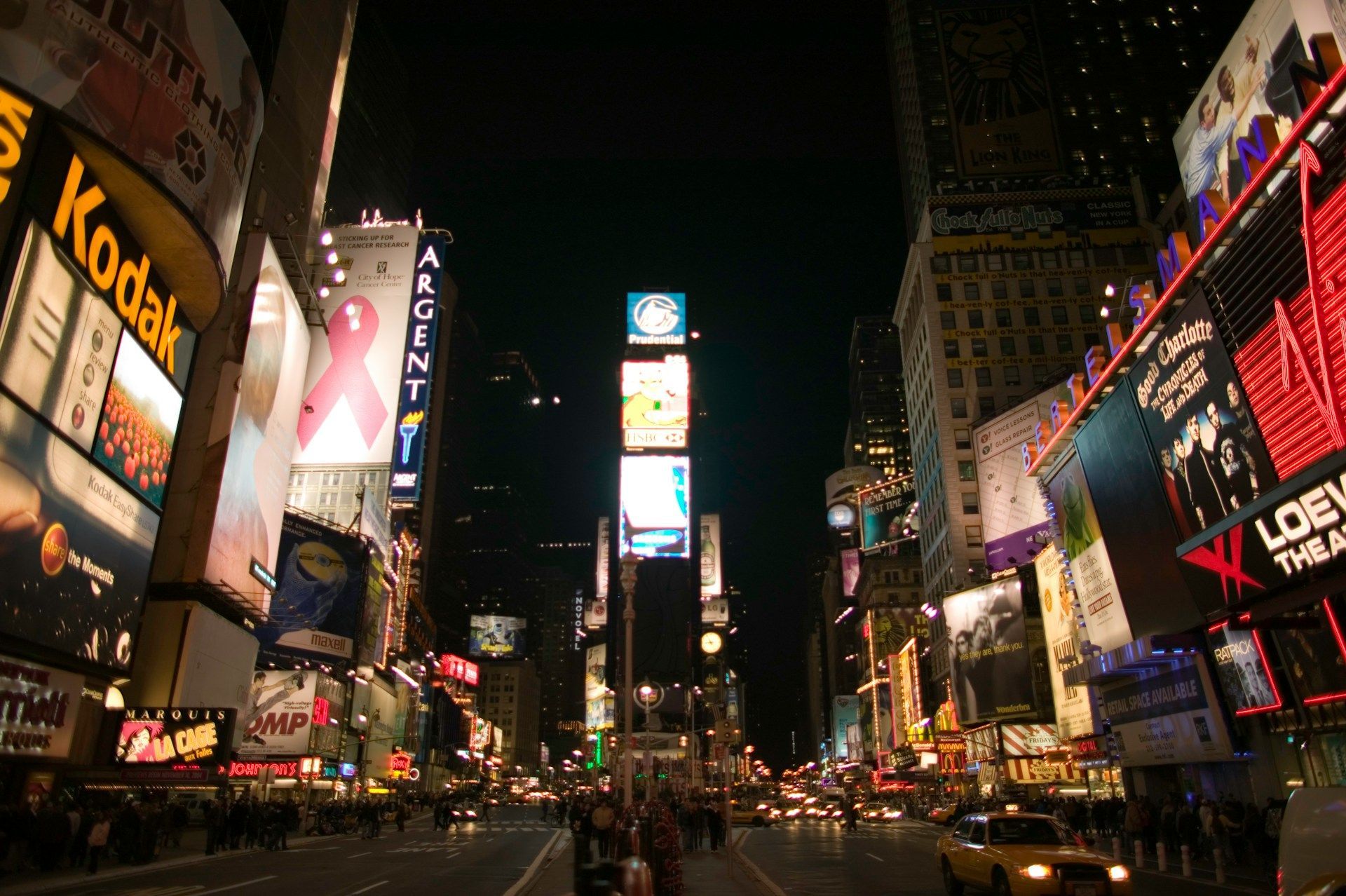 A busy city street at night with a kodak sign in the foreground