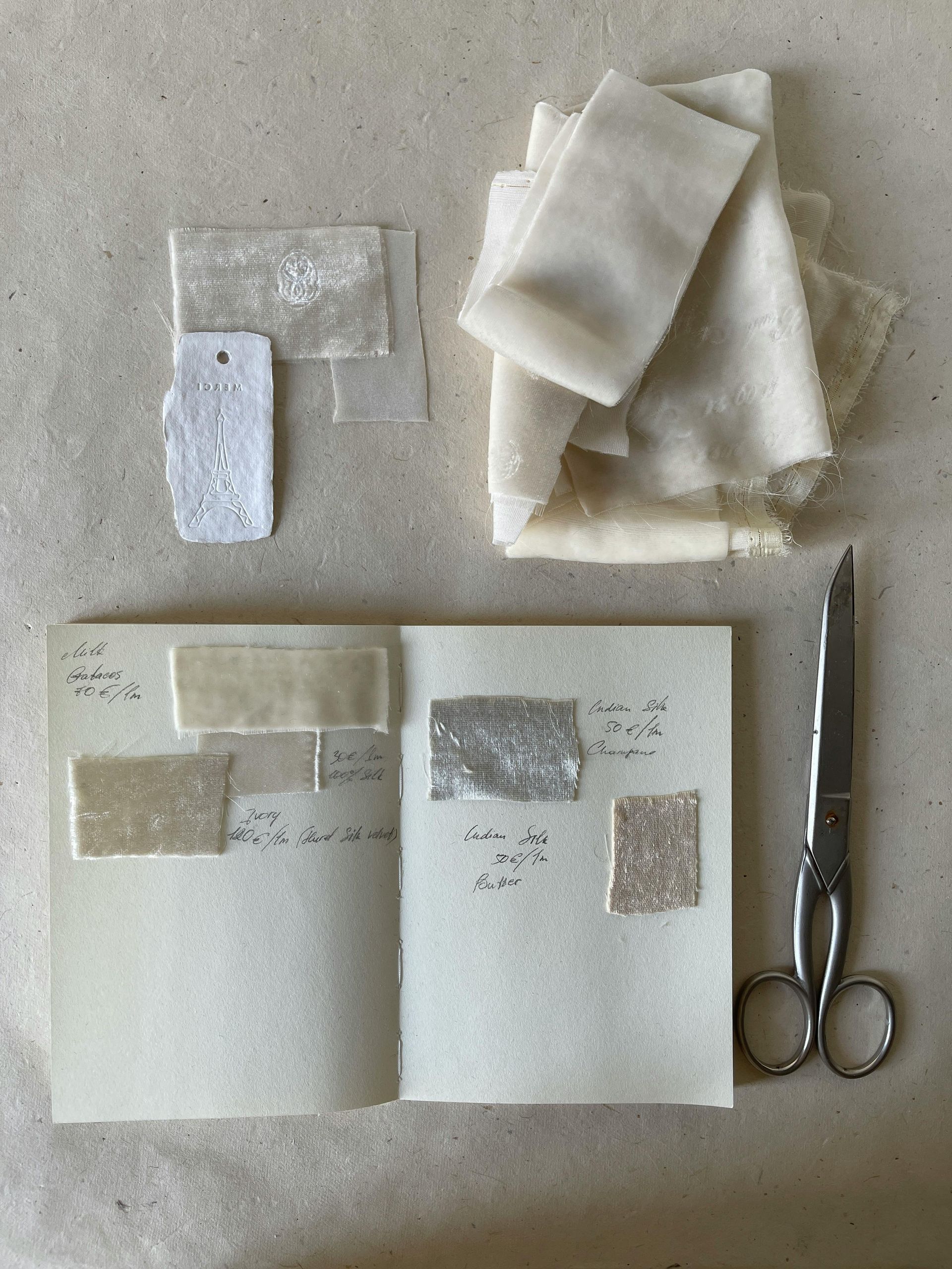 A pair of scissors is sitting next to a notebook filled with fabric samples.