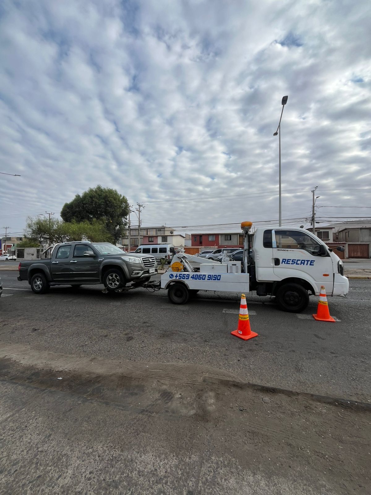 Un operario de servicio con uniforme azul y guantes negros abre la puerta de un coche plateado en una carretera, con una furgoneta al fondo.