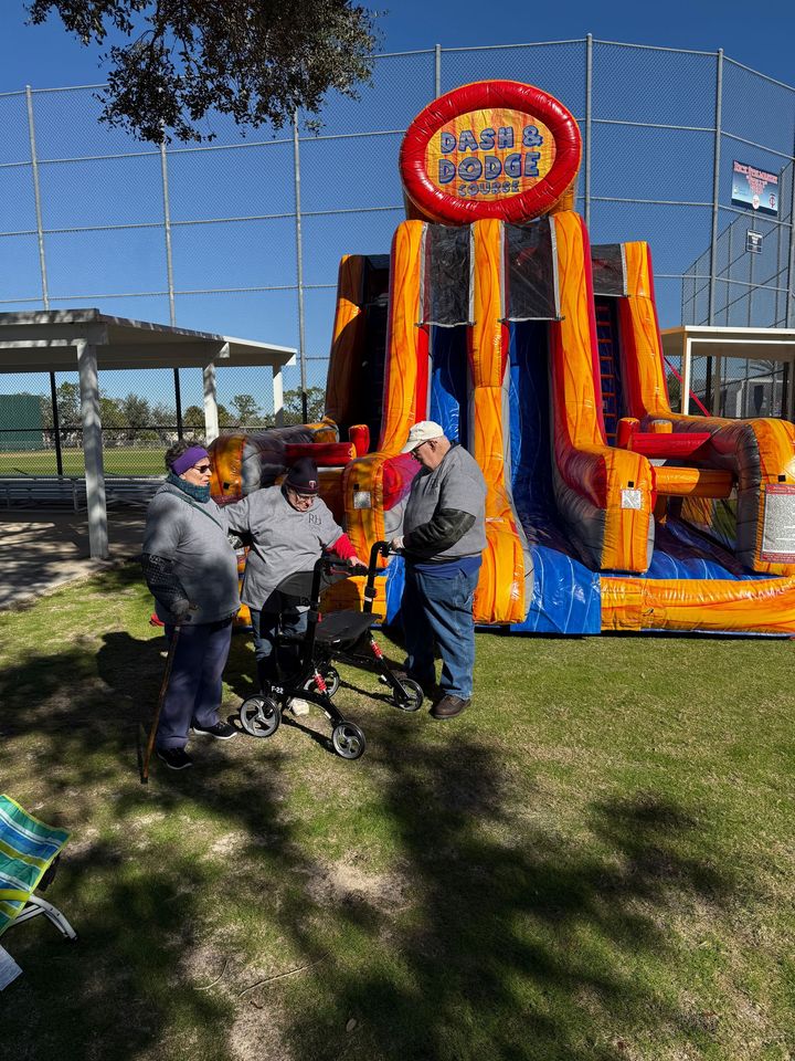 Three people at an inflatable slide; one in a wheelchair. Outdoor setting on a sunny day.