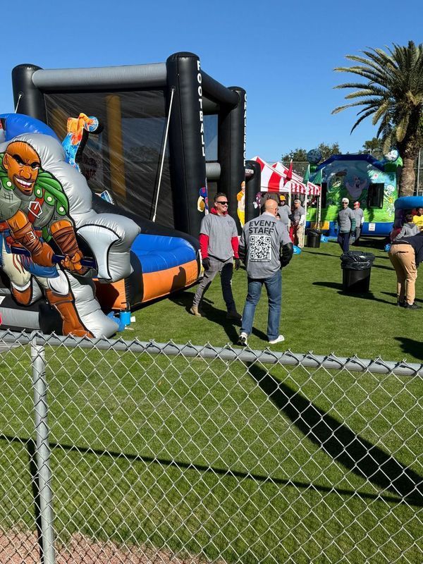 Outdoor event with inflatable structures, people on grass, sunny day.
