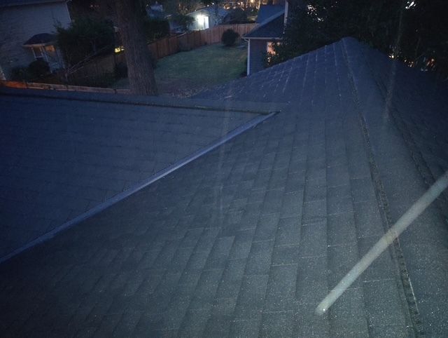 Dimly lit rooftop with gray shingles at dusk, with nearby houses and streetlights in the background