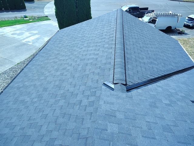 Gray shingled roof with a ridge vent, viewed from above in a parking lot area