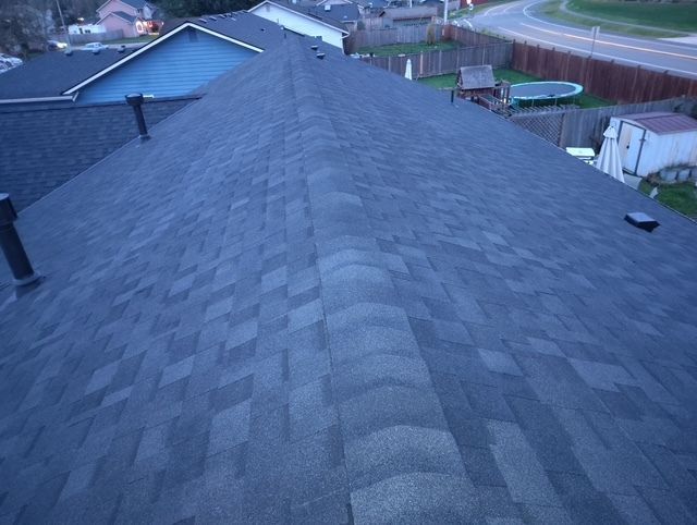 Dark gray shingled roof viewed from the ridge toward a suburban street at dusk.