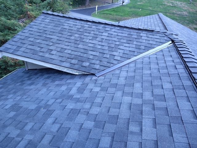 Roof shingles with a damaged ridge cap and lifted roof section, viewed from above