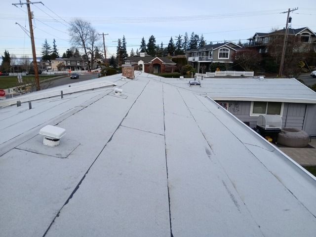 View from a rooftop over white shingles toward houses and trees on a cloudy day