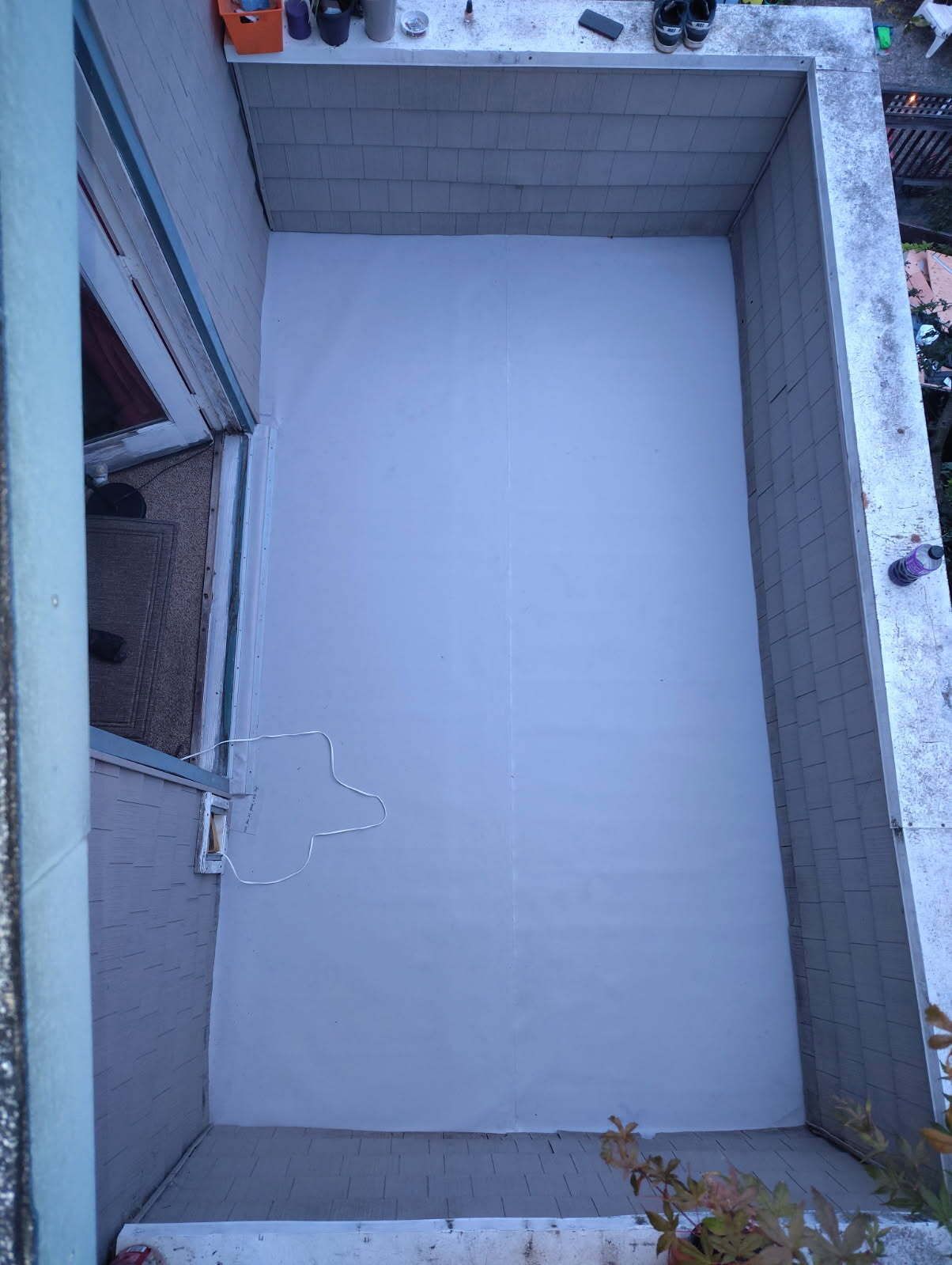 Small empty concrete balcony with light gray tiled floor and walls, viewed from above.