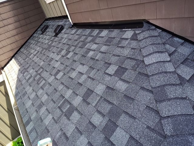 Gray asphalt shingle roof with skylights next to a brown house wall