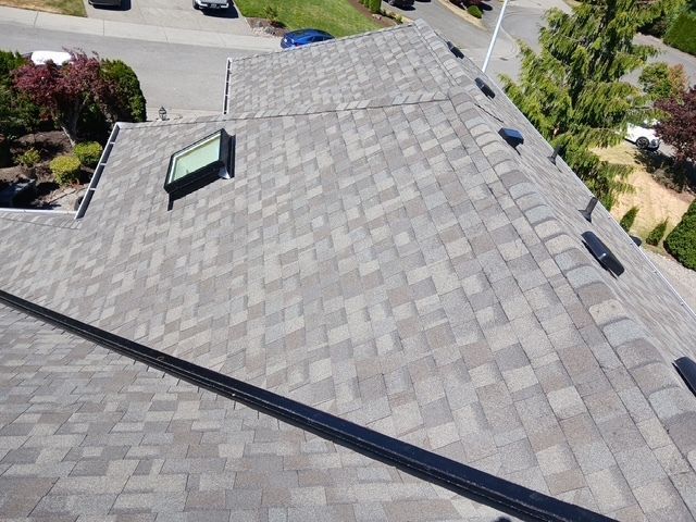 Aerial view of a gray shingled roof with a skylight and nearby street.