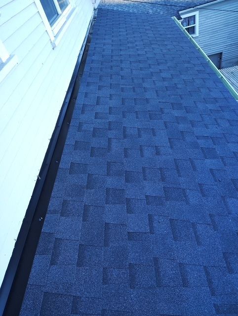 Blue shingled roof with a narrow black ridge beside white siding, viewed from below