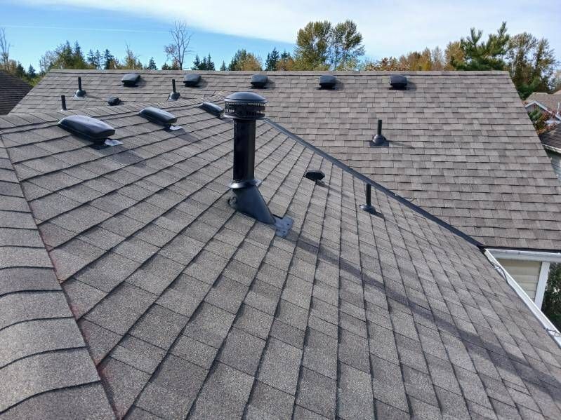 Gray shingled roof with vents and a chimney under a blue sky