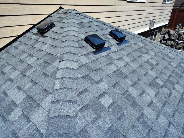 Gray shingled roof with three black vents beside beige siding