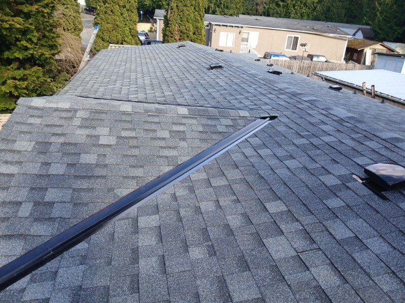 Roof covered in gray shingles with a long roof vent and a small satellite dish on the right.