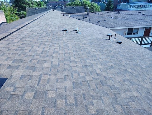 The roof of a house with a balcony and trees in the background.