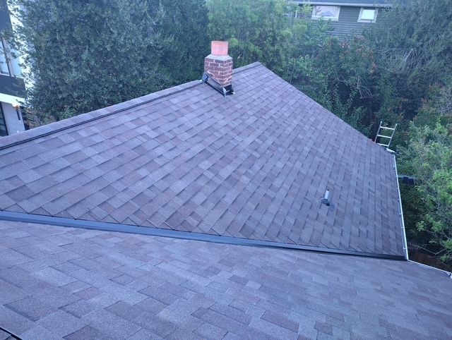Roofing shingles on a house with a brick chimney, viewed from above with trees in the background