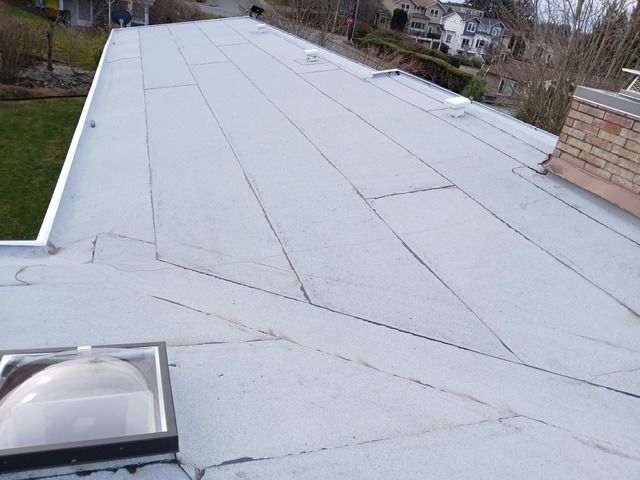 Flat gray rooftop with seams and a skylight, viewed from above on a residential building.