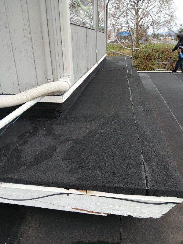 Damaged black rooftop ramp beside a white building, with peeling edge and a person in the background