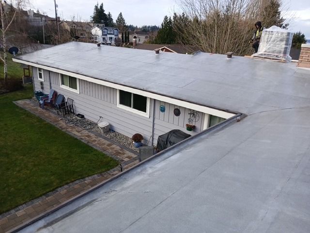Single-story house with a flat gray roof and stone chimney, viewed from above in a wooded neighborhood