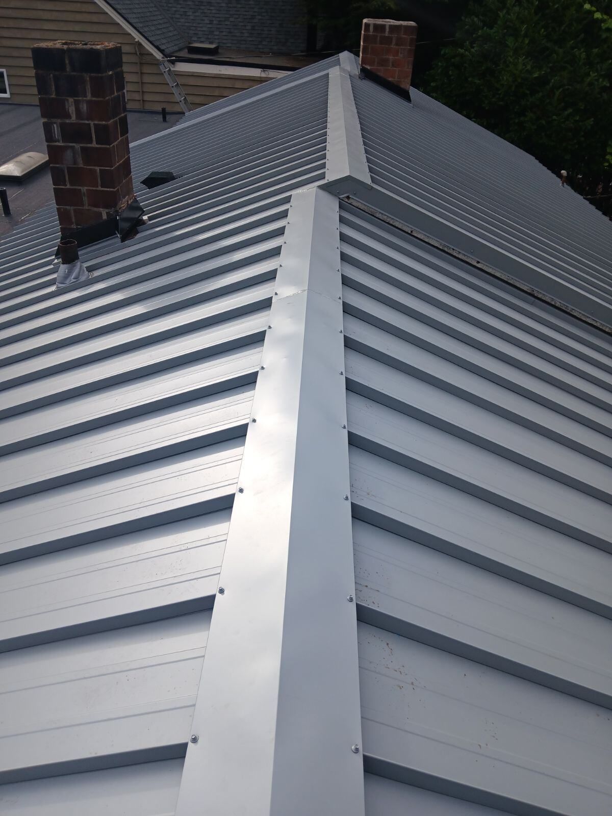 Metal rooftop with gray standing-seam panels and two brick chimneys viewed from above