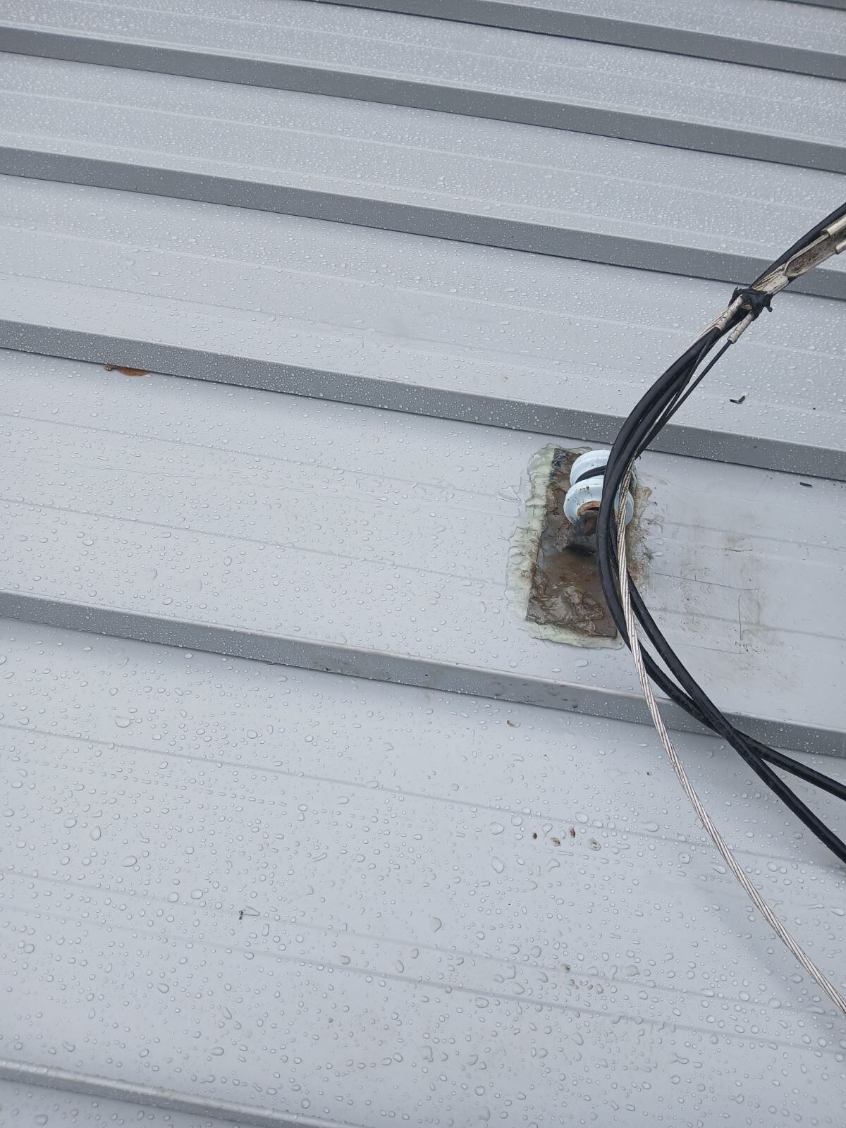 Close-up of a roof cable entering through a rusted metal mounting point on corrugated siding
