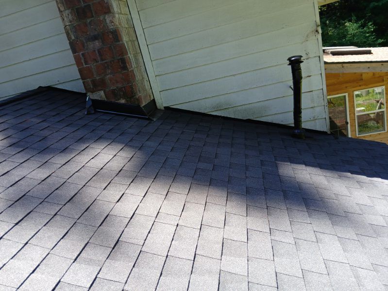 Rooftop with gray shingles, brick chimney, white siding, and strong sunlight casting shadows