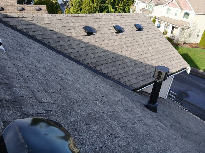 Roof with gray asphalt shingles, three roof vents, and a chimney on a suburban house.