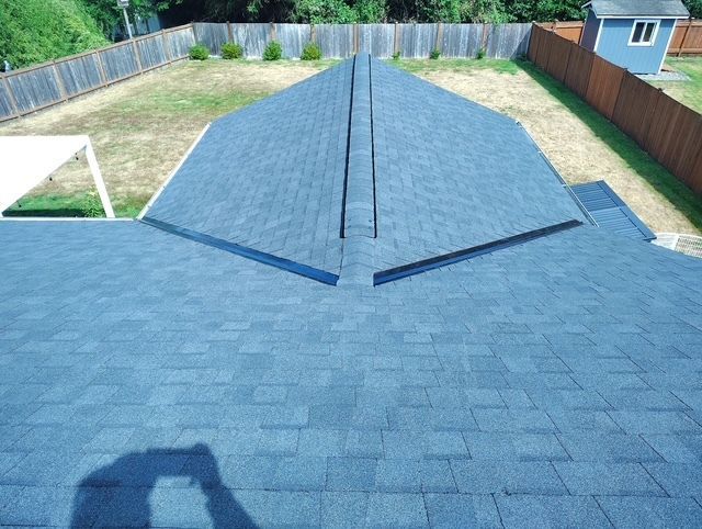 Blue shingle roof viewed from above with a central ridge and fenced backyard beyond