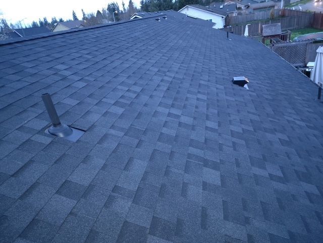 Rooftop covered in gray shingles with two vent pipes and a small skylight, viewed at dusk