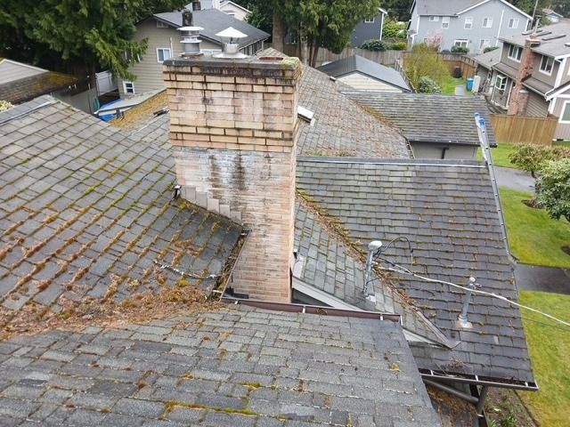 Rooftops with weathered gray shingles and a brick chimney in a residential neighborhood