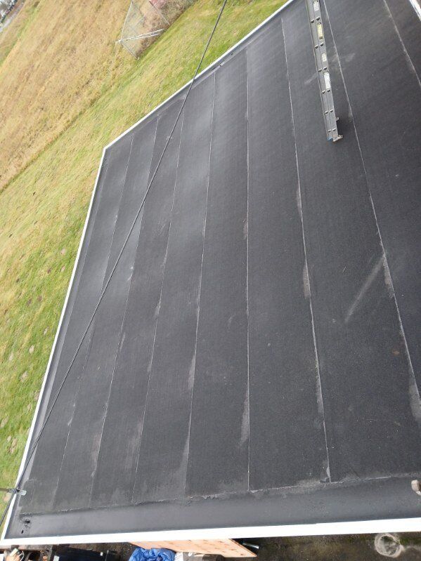 Black tarp-covered surface on a sloped roof beside a grassy yard